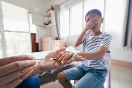 Asian child girl feeling scared while parent helping her perform first aid finger injury after she has been an accident.の写真素材