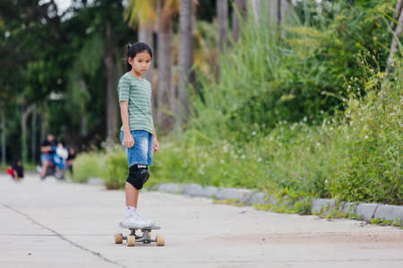 Asian child girl learning to skateboard outdoors. Kid having fun and playing skateboard on the road at the day time. Kid activity and extreme sport concept.の写真素材
