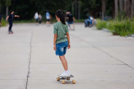 Asian child girl learning to skateboard outdoors. Kid having fun and playing skateboard on the road at the day time. Kid activity and extreme sport concept.の写真素材