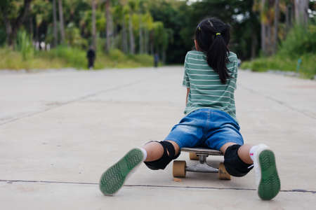 Asian child girl learning to skateboard outdoors. Kid having fun and playing skateboard on the road at the day time. Kid activity and extreme sport concept.の写真素材