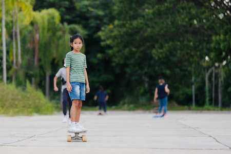 Asian child girl learning to skateboard outdoors. Kid having fun and playing skateboard on the road at the day time. Kid activity and extreme sport concept.の写真素材