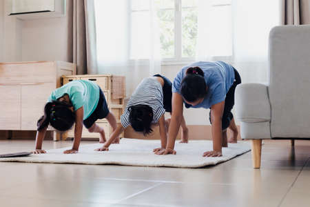 Asian young mother and her daughters doing stretching fitness exercise yoga together at home. Parent and children work out to be strong and maintain physical health and wellbeing in daily routine.の写真素材