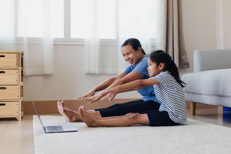 Asian young mother and her daughter doing stretching fitness exercise yoga together at home. Parent teaching child work out to be strong and maintain physical health and wellbeing in daily routine.の写真素材