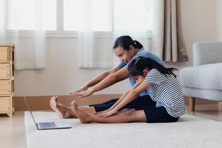 Asian young mother and her daughter doing stretching fitness exercise yoga together at home. Parent teaching child work out to be strong and maintain physical health and wellbeing in daily routine.の写真素材