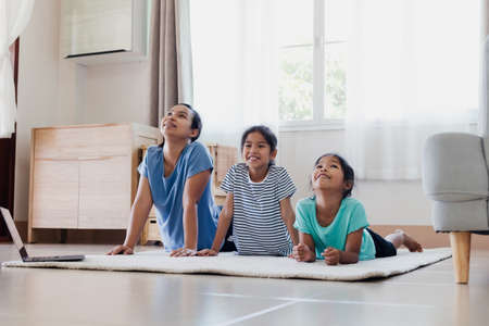 Asian young mother and her daughters doing stretching fitness exercise yoga together at home. Parent and children work out to be strong and maintain physical health and wellbeing in daily routine.の写真素材
