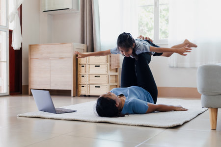 Asian young mother and her daughter doing stretching fitness exercise yoga together at home. Parent teaching child work out to be strong and maintain physical health and wellbeing in daily routine.の写真素材