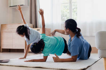 Asian young mother and her daughters doing stretching fitness exercise yoga together at home. Parent and children work out to be strong and maintain physical health and wellbeing in daily routine.の写真素材