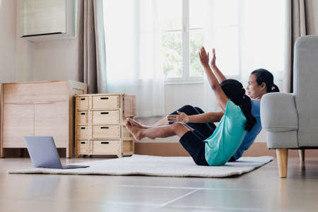 Asian young mother and her daughter doing stretching fitness exercise yoga together at home. Parent teaching child work out to be strong and maintain physical health and wellbeing in daily routine.の写真素材