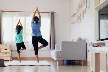 Asian young mother and her daughter doing stretching fitness exercise yoga together at home. Parent teaching child work out to be strong and maintain physical health and wellbeing in daily routine.の写真素材