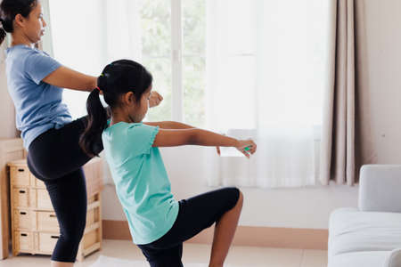 Asian young mother and her daughter doing stretching fitness exercise yoga and using the bottle of water to be dumbbells together at home in daily routine.の写真素材