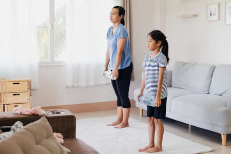 Asian young mother and her daughter doing stretching fitness exercise yoga and using the bottle of water to be dumbbells together at home in daily routine.の写真素材