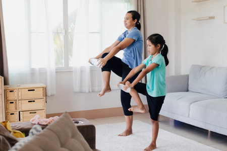 Asian young mother and her daughter doing stretching fitness exercise yoga and using the bottle of water to be dumbbells together at home in daily routine.の写真素材