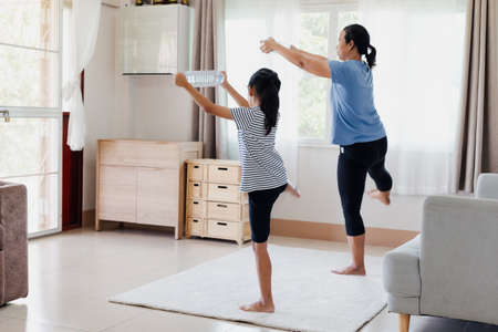 Asian young mother and her daughter doing stretching fitness exercise yoga and using the bottle of water to be dumbbells together at home in daily routine.の写真素材