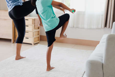 Asian young mother and her daughter doing stretching fitness exercise yoga and using the bottle of water to be dumbbells together at home in daily routine.の写真素材