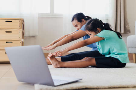 Asian young mother and her daughter doing stretching fitness exercise yoga together at home. Parent teaching child work out to be strong and maintain physical health and wellbeing in daily routine.の写真素材