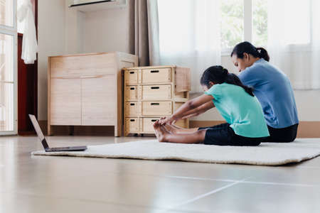 Asian young mother and her daughter doing stretching fitness exercise yoga together at home. Parent teaching child work out to be strong and maintain physical health and wellbeing in daily routine.の写真素材