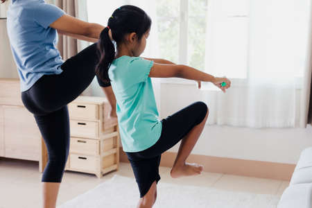 Asian young mother and her daughter doing stretching fitness exercise yoga and using the bottle of water to be dumbbells together at home in daily routine.の写真素材