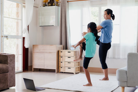 Asian young mother and her daughter doing stretching fitness exercise yoga and using the bottle of water to be dumbbells together at home in daily routine.の写真素材
