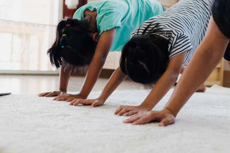 Asian young mother and her daughters doing stretching fitness exercise yoga together at home. Parent and children work out to be strong and maintain physical health and wellbeing in daily routine.の写真素材