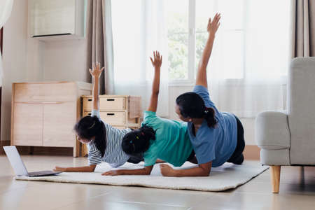Asian young mother and her daughters doing stretching fitness exercise yoga together at home. Parent and children work out to be strong and maintain physical health and wellbeing in daily routine.の写真素材