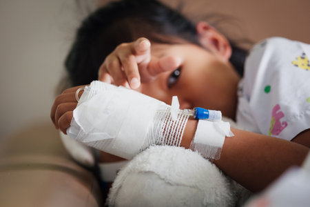 Sick kid feeling unwell lying down and hugging her doll in the bed while stay in private patient rooms in the hospital. Healthcare and lifestyle concept.の写真素材