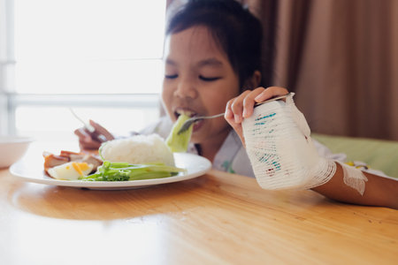 Sick asian child girl eating healthy food for lunch by herself while stay in private patient rooms in the hospital. Healthcare and lifestyle concept.の写真素材