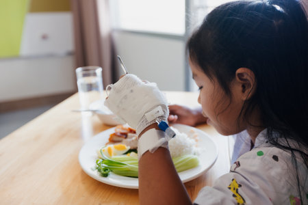 Sick asian child girl eating healthy food for lunch by herself while stay in private patient rooms in the hospital. Healthcare and lifestyle concept.の写真素材