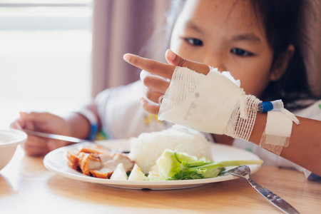 Sick asian child girl eating healthy food for lunch by herself while stay in private patient rooms in the hospital. Healthcare and lifestyle concept.の写真素材