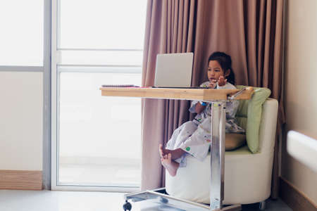 Sick asian child sitting and learning online class with teacher and friend while stay in private patient rooms in the hospital. Isolation homeschooling and distance learning.の写真素材