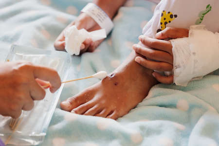 Close up on mother helping her sick daughter cleaning and putting medicine on her wound while stay in private patient rooms in the hospital. Healthcare and lifestyle concept.の写真素材