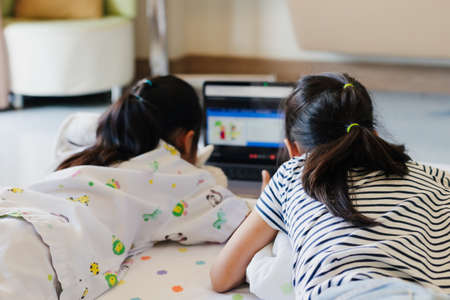 Sick asian child feel bored and lying on bed with her sister while learning online class with teacher and friend when stay in the hospital. Isolation homeschooling and distance learning.の写真素材