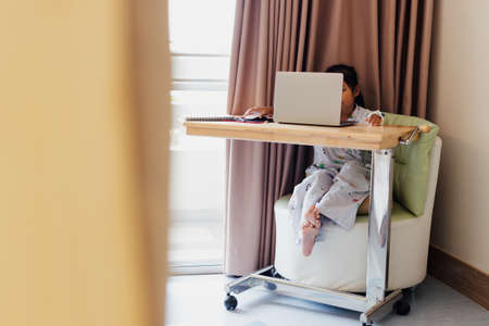 Sick asian child sitting and learning online class with teacher and friend while stay in private patient rooms in the hospital. Isolation homeschooling and distance learning.の写真素材