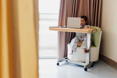 Sick asian child sitting and learning online class with teacher and friend while stay in private patient rooms in the hospital. Isolation homeschooling and distance learning.の写真素材