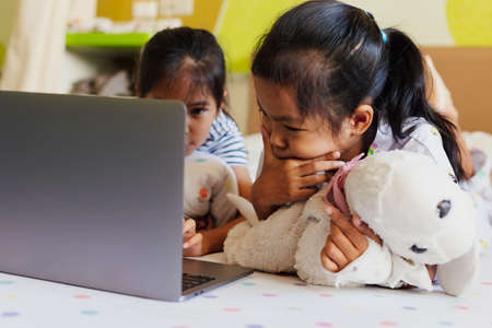 Sick asian child feel bored and lying on bed with her sister while learning online class with teacher and friend when stay in the hospital. Isolation homeschooling and distance learning.の写真素材