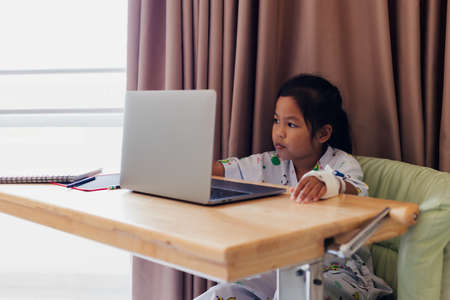 Sick asian child sitting and learning online class with teacher and friend while stay in private patient rooms in the hospital. Isolation homeschooling and distance learning.の写真素材
