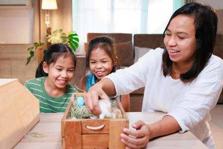 Asian mother and her daughters are playing with baby bunny and decorating easter eggs preparing for Easter at home. Happy family Happy easter Happy holiday.の写真素材