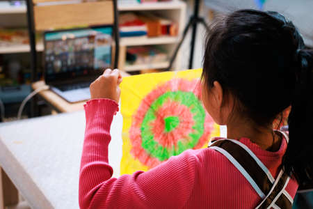 Asian child girl enjoy making tie dye cloth at home. Kid show her finish tie dye cloth to her teacher and friend while online learning. Art and craft DIY for kid concept.の写真素材