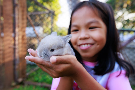 Asian child girl holding cute baby bunny on hand with love and tenderness. Kid and her pet playing together.の写真素材