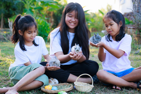 Group of asian girls friendship holding adorable bunny fluffy in hand playing with baby rabbits in the garden with tenderness and love. People take care and play with a pet.の写真素材