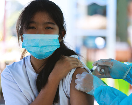 Asian child girl in face mask receiving covid-19 vaccine injection at health centre. Kids approving of coronavirus immunization, being protected against Covid-19 virus.の写真素材