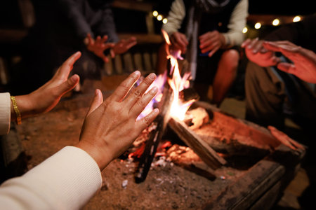 Close-up on hand of woman warming on campfire. Group of asian friends sitting around campfire in the...
