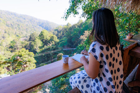 Asian woman sitting on balcony and writing idea on notebooks near fresh nature with hot drink in the morning time.の写真素材