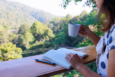 Asian woman sitting on balcony and writing idea on notebooks near fresh nature with hot drink in the morning time.の写真素材