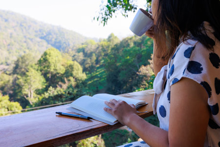Asian woman sitting on balcony and writing idea on notebooks near fresh nature with hot drink in the morning time.の写真素材