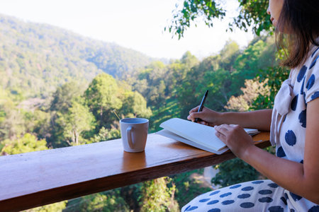 Asian woman sitting on balcony and writing idea on notebooks near fresh nature with hot drink in the morning time.の写真素材
