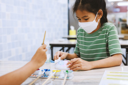 Asian child girl using paint brush is painting on ceramic bowl with oil color. Kids arts and crafts creative activity class in workshop. DIY for kids, home activities, handmade decorations.の写真素材