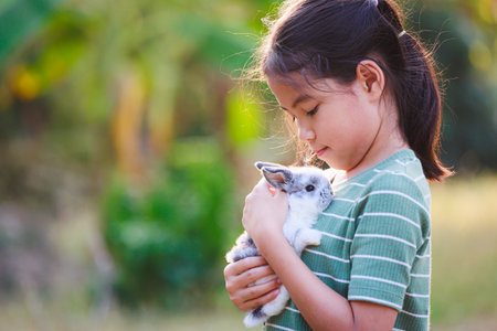 Asian child girl holding and hugging her adorable bunny fluffy with tenderness and love. Kid take care and play with pet in the garden. Symbol of Easter day.の写真素材