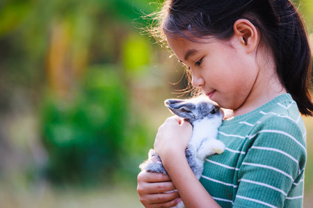 Asian child girl holding and hugging her adorable bunny fluffy with tenderness and love. Kid take care and play with pet in the garden. Symbol of Easter day.の写真素材