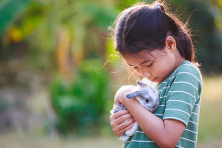Asian child girl holding and hugging her adorable bunny fluffy with tenderness and love. Kid take care and play with pet in the garden. Symbol of Easter day.の写真素材