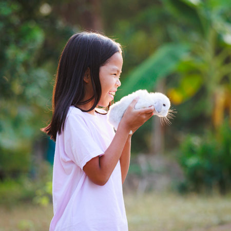 Asian child girl holding and hugging her adorable bunny fluffy with tenderness and love. Kid take care and play with pet in the garden. Symbol of Easter day.の写真素材